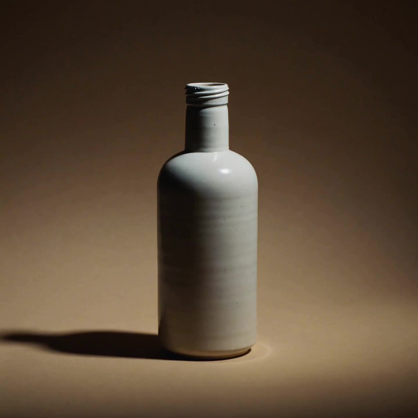 An unbranded matte ceramic bottle on a warm gradient studio backdrop.
