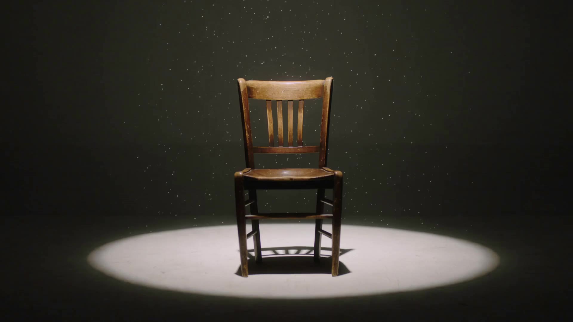 An empty film set lit by a single spotlight on a wooden chair, dust drifting through the beam.