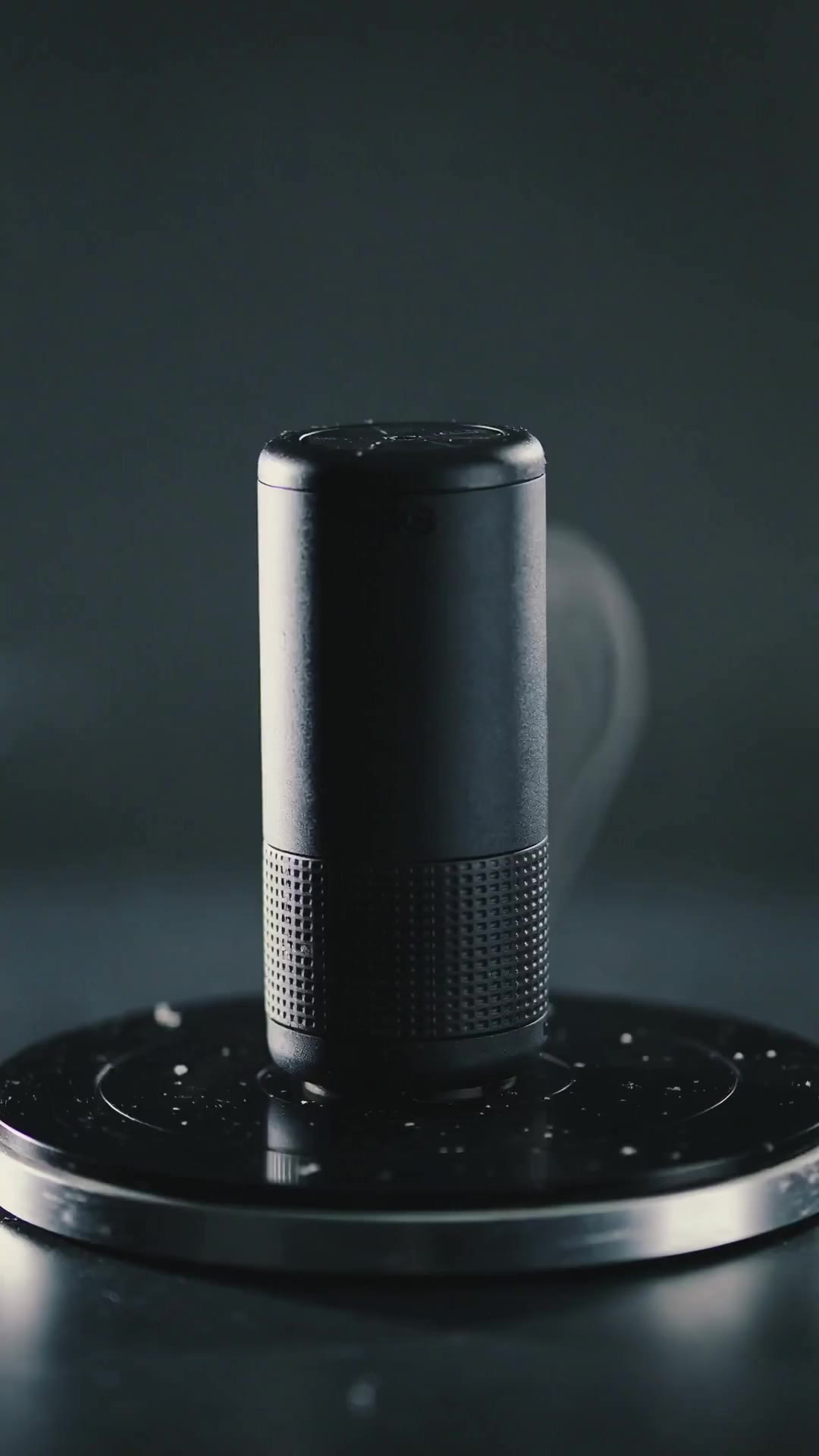 An unbranded portable speaker rotating on a dark reflective turntable under dramatic rim light.