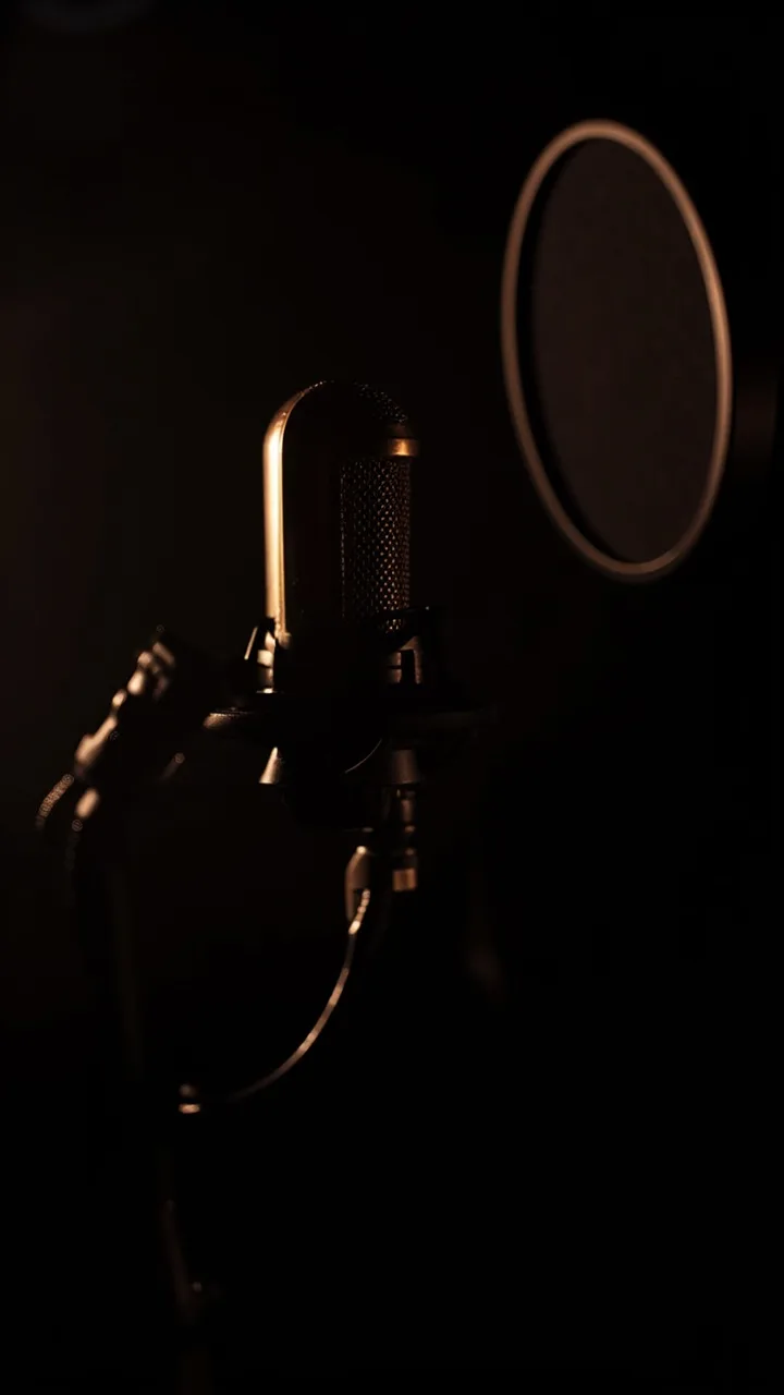 A microphone on a boom arm in a dark podcast studio.